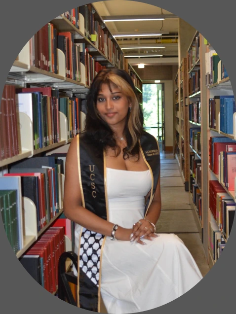 Pehara in a UCSC graduation stole, sitting between library shelves